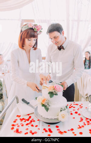 Charming bride and handsome groom are cutting a wedding cake. Couple in the restaurant with white pie Stock Photo