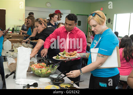 Adult volunteers serve themselves salad in cafeteria during after-school activity at middle school in Austin, Texas Stock Photo