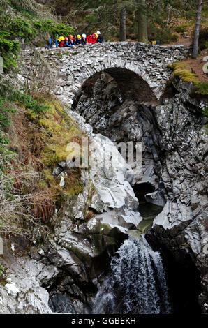 A colourful group of abseilers looking over the parapet of the lower bridge at the Falls of Bruar in the Scottish Highlands. Stock Photo