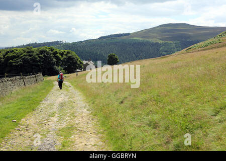 Female hiker walking along the path round Crook HIll, which can be seen rising to the right, in the Peak District, England, UK Stock Photo