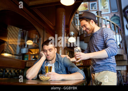 man with beer and drunk friend at bar or pub Stock Photo