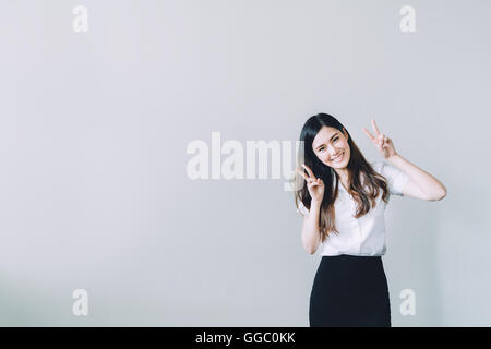 Cute asian university girl doing funny rabbit pose, copy space on gray wall background Stock Photo