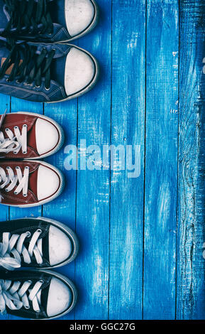 Three pairs of old sneakers on a blue shabby wooden vertical background, top view Stock Photo