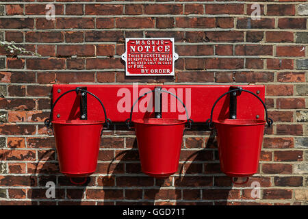 Red fire buckets hanging on hooks in a row of three, at an old 1940's railway station platform Stock Photo