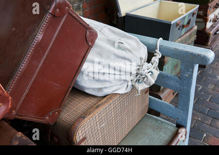 Old suitcases at a steam railway station stacked on a barrow cart, on the platform Stock Photo