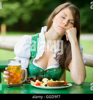 young woman in dirndl sleeping at table in beer garden and holding a beer mug Stock Photo