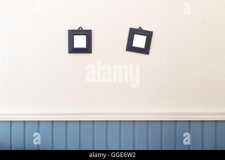 Two small square frames hanging on the white and blue wall. Stock Photo