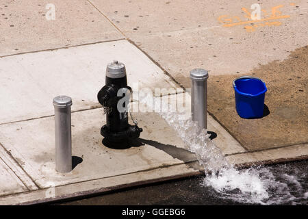 Open Fire Hydrant on the sidewalk shooting a stream of water into the street on a hot summer day Stock Photo