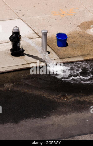 Open Fire Hydrant on the sidewalk shooting a stream of water into the street on a hot summer day Stock Photo