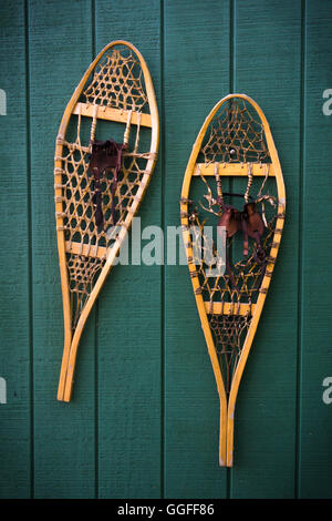 A pair of traditional teardrop snowshoes mounted on a green wooden wall Stock Photo