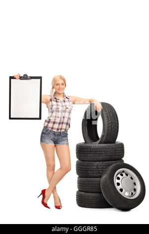 Vertical shot of a female mechanic holding a blank clipboard and posing by a stack of tires isolated on white background Stock Photo