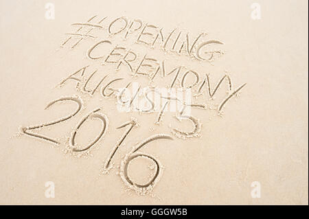 RIO DE JANEIRO - MARCH 20, 2016: Opening Ceremony message handwritten with social media hashtag on smooth sand beach. Stock Photo
