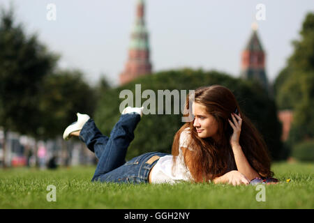 Portrait of young beautiful woman lying on grass and speaking on telephone at summer green park Stock Photo