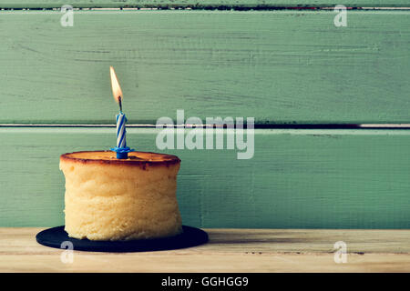 a cheesecake topped with a lit birthday candle, on a rustic wooden surface against a rustic pale green wooden background Stock Photo