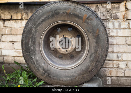 Old used car wheel stands near grungy brick wall Stock Photo