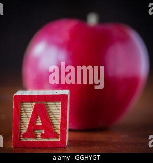 A child's wooden block with the letter A and an apple defocused in the background. Stock Photo