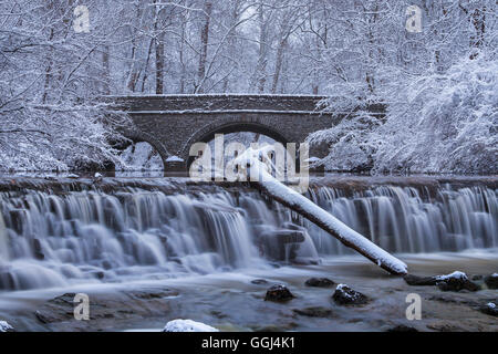 Snow Covered Trees Framing A Stone Bridge And Waterfall During Winter In The Park, Sharon Woods, Southwestern Ohio, USA Stock Photo