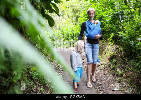 Mother hiking with her kids, baby 5 months, wrap, baby sling, son 3 years old, tropical rain forest, walking, family travel in A Stock Photo