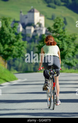 Woman cycling along road, castle of Tarasp in background, Ftan, Lower Engadin, Engadin, Grisons, Switzerland Stock Photo