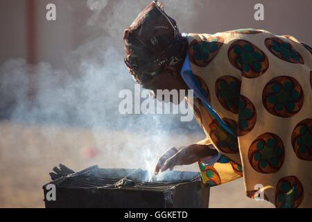 Herero woman bending over a smoking grill, Sesfontain, Namibia Stock Photo