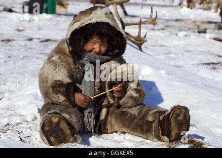 Nomad girl dressed in reindeer skins, sitting in the snow, Chukotka Autonomous Okrug, Siberia, Russia Stock Photo