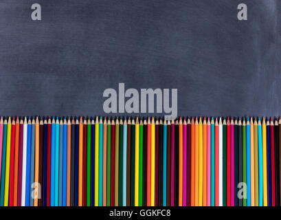 Overhead view of colorful pencils lined up on bottom of erased chalkboard. Stock Photo