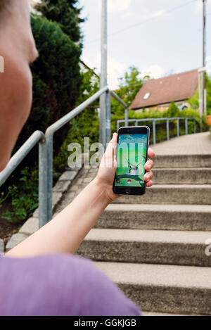 Ostfildern, Germany - July 17, 2016: A woman is playing the augmented reality smartphone app 'Pokemon GO' on her iPhone while ou Stock Photo