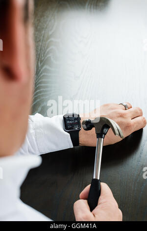 Ostfildern, Germany - July 31, 2016: A businessman wearing a white shirt is destroying the Apple Watch on his wrist using a hamm Stock Photo