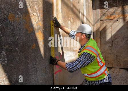 Caucasian construction worker holding level against wall Stock Photo