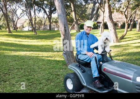 Older Caucasian man on riding lawnmower with pet dog Stock Photo
