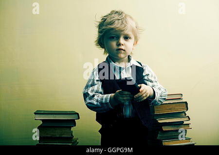 Boy holding cell phone near stacks of books Stock Photo