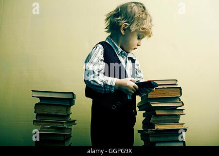 Boy holding cell phone near stacks of books Stock Photo