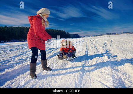 Mother and sons sledding in snowy remote field Stock Photo