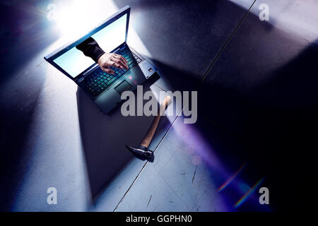 Hand of hacker reaching from screen of laptop and typing Stock Photo