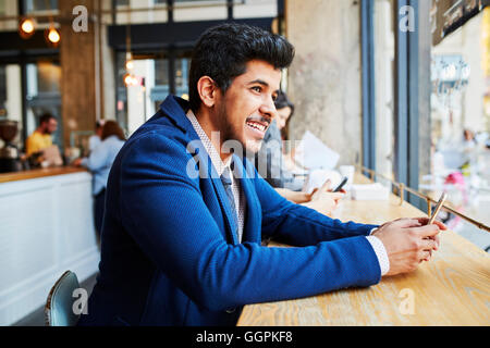 Smiling Middle Eastern man using cell phone at cafe window Stock Photo