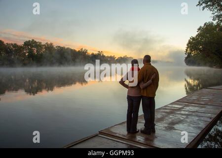 Older couple hugging at foggy river at sunrise Stock Photo