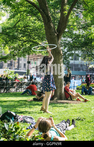 young woman in print dress hair flying plays with hula hoop on spring green grass of Union Square as girl friend snaps picture Stock Photo