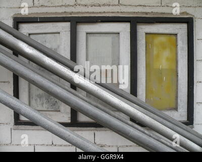 Old weathered and worn window shutters fronted by random lengths of metal pipe running top left to bottom right in photo. Stock Photo
