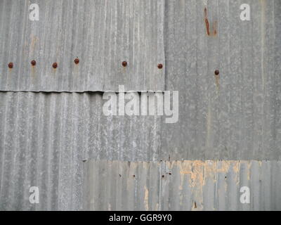 Sections of overlapping, old rusty sheet metal panels adorned with rusty nail heads. Stock Photo