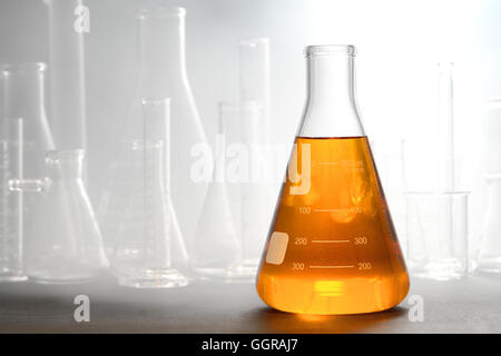 Scientific laboratory glass conical Erlenmeyer flask filled with amber orange chemical liquid with glassware equipment in smoke Stock Photo