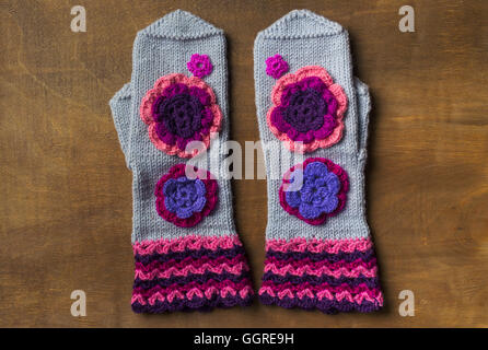 Gray mittens handmade on wooden surface with flowers. Flat lay Stock Photo