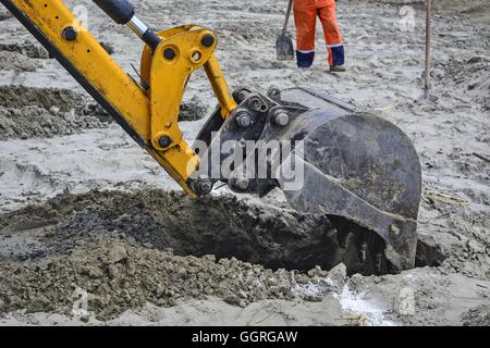 Excavator in a situation digs holes in the sandy ground. Stock Photo
