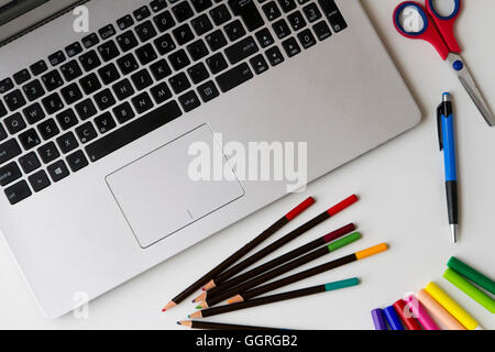 Laptop PC and some objects such as pen, colored pencils, felt tip pens, scissors on white table. Top view. Flat lay. Stock Photo