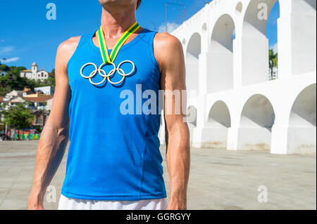 RIO DE JANEIRO - MARCH 6, 2015: Athlete wearing Olympic rings gold medal stands outdoors in the plaza in front of Lapa Arches. Stock Photo