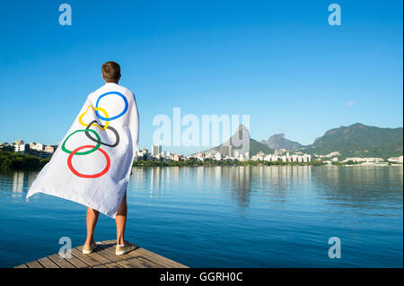 RIO DE JANEIRO - MARCH 27, 2016: Athlete stands draped in Olympic flag in front of Lagoa Rodrigo da Freitas Lagoon. Stock Photo