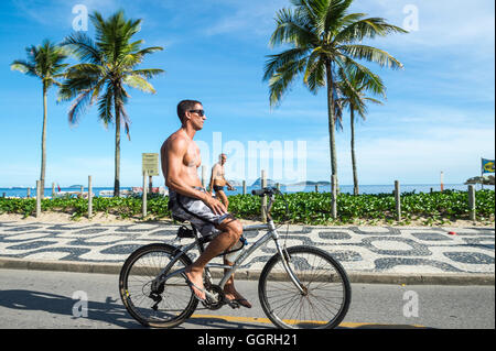 RIO DE JANEIRO - FEBRUARY 28, 2016: Brazilian man rides bicycle along the Ipanema Beach beachfront bike path. Stock Photo