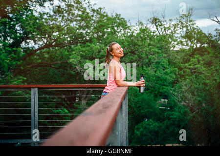 Caucasian woman leaning on banister holding water bottle Stock Photo