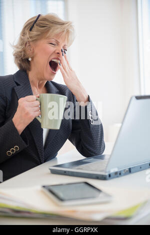 Fatigued Caucasian businesswoman drinking coffee and yawning Stock Photo