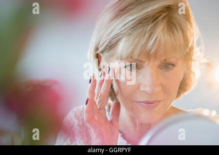 Older Caucasian woman applying moisturizer to face Stock Photo