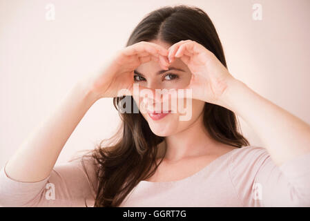 Caucasian woman gesturing heart-shape with hands over eyes Stock Photo